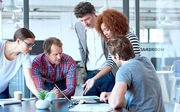 Five co-workers discussing space technology at a desk in front of a laptop